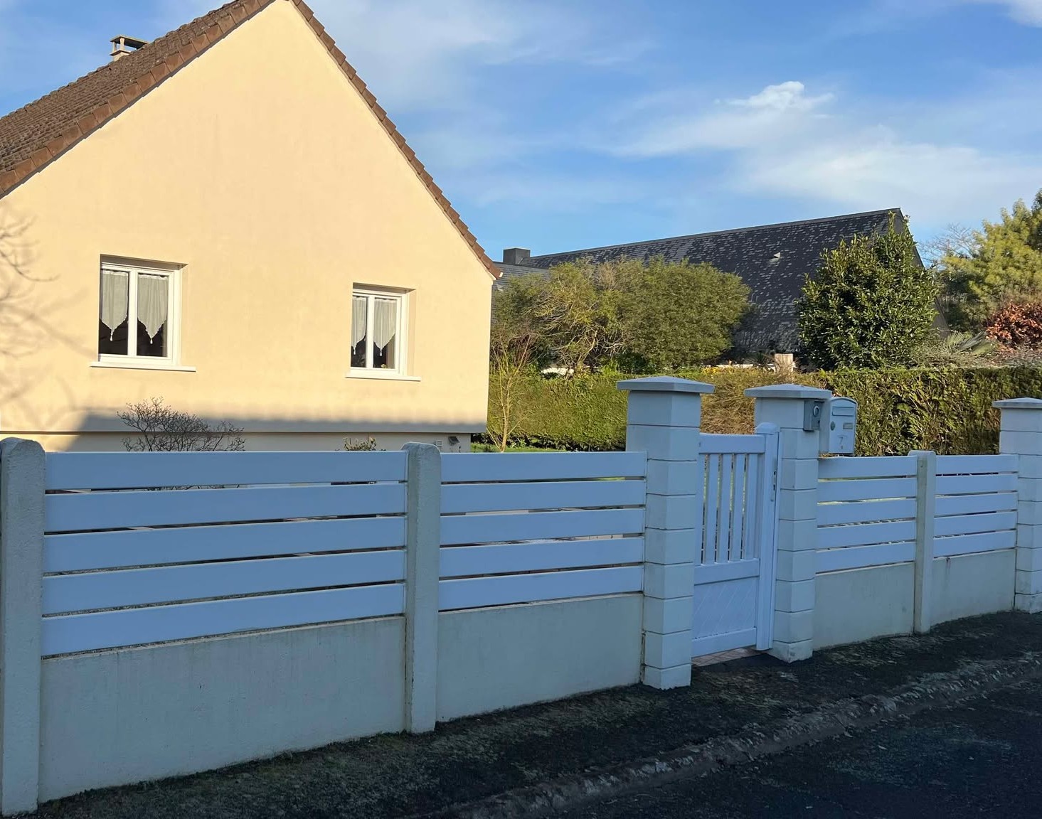 Portail en PVC blanc avec clôture à lattes, intégrée à des pilastres en béton.