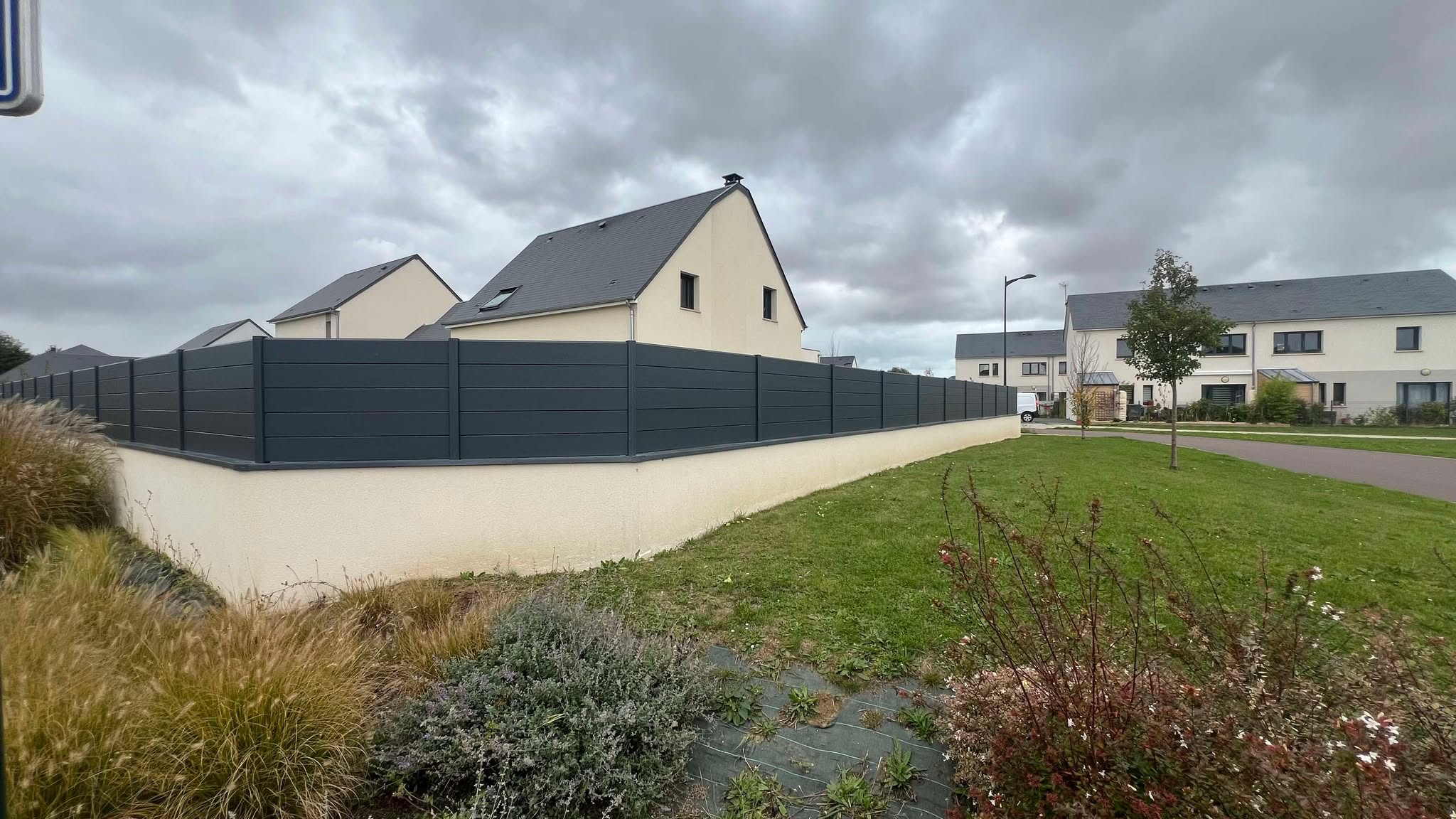 Clôture en composite gris, avec lames horizontales, installée autour d'un jardin.