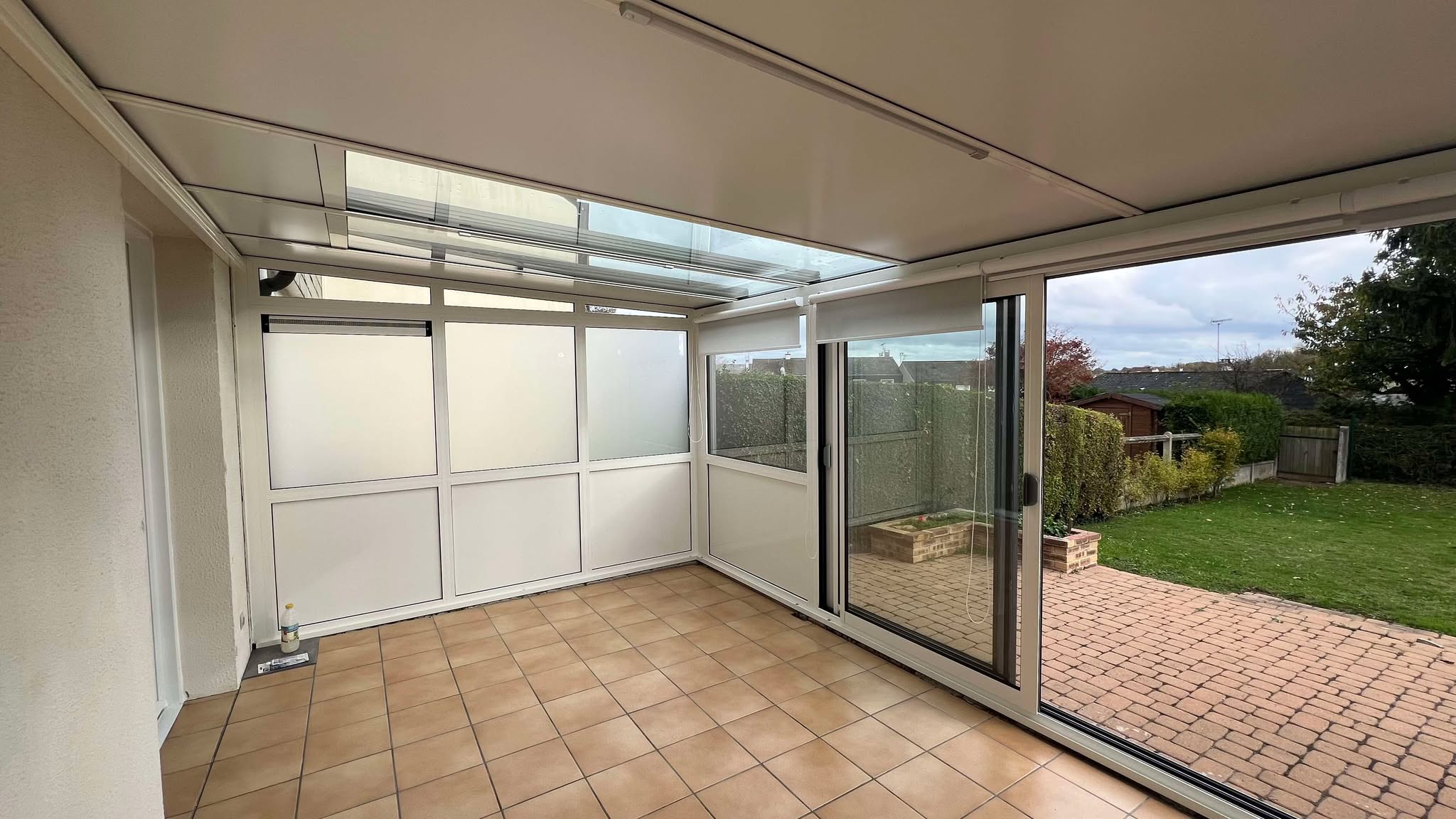 Véranda en aluminium avec grandes baies vitrées et toiture vitrée, sol en carrelage beige.