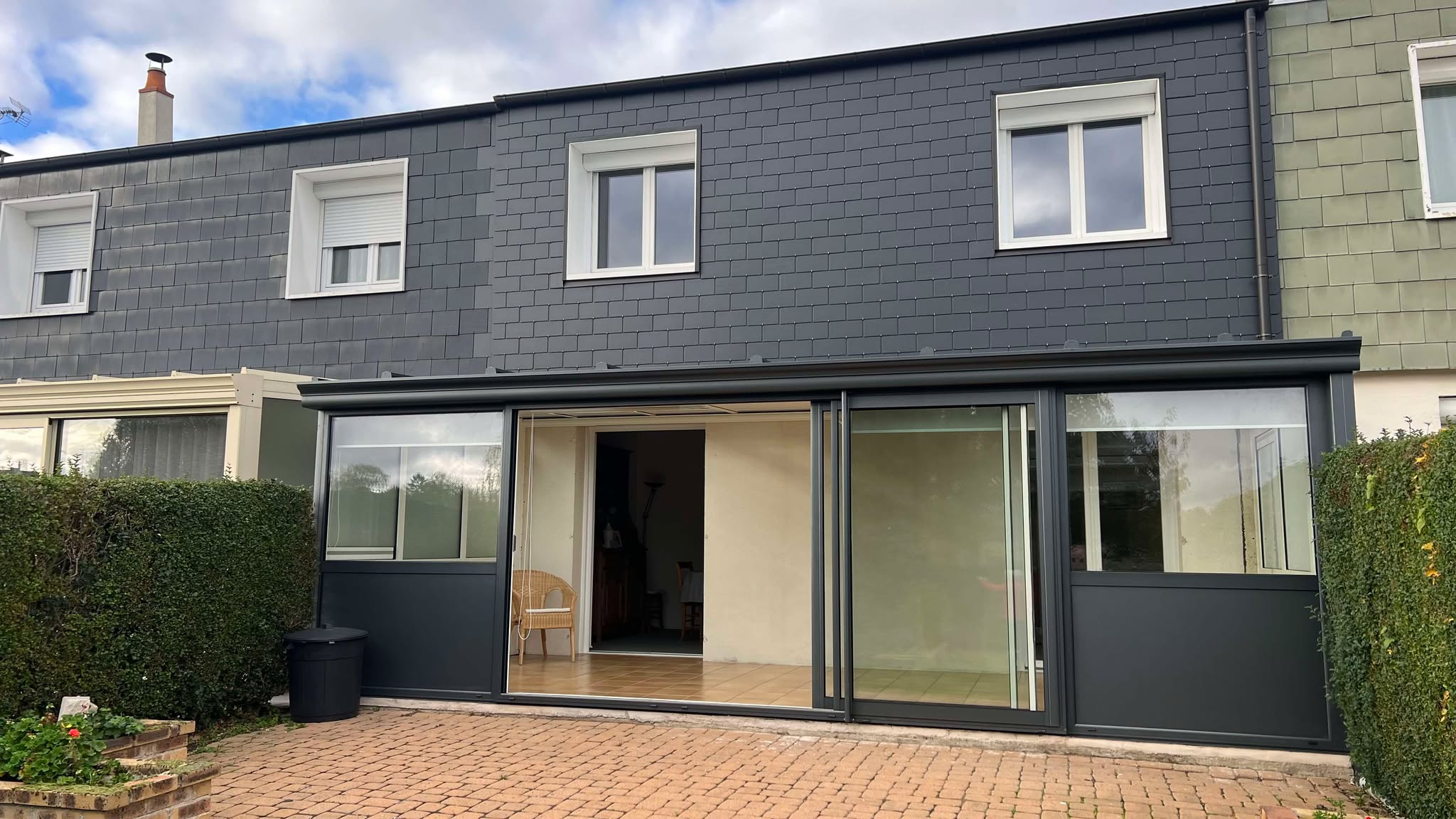 Véranda en aluminium avec baies vitrées, finition noire, posée sur une structure existante.