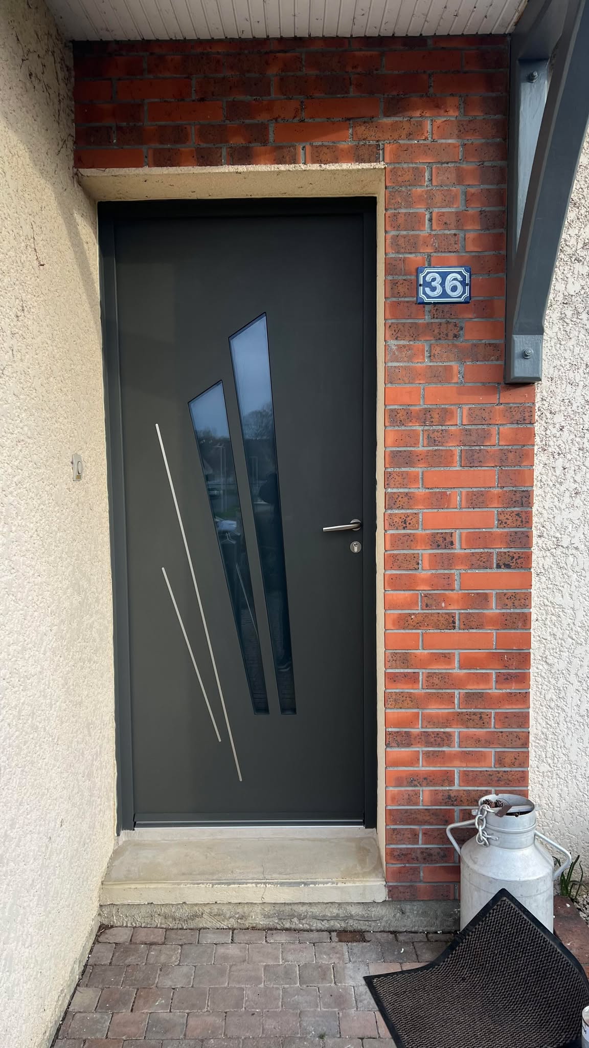 Porte d'entrée en aluminium gris avec vitrage décoratif, dotée de motifs géométriques.