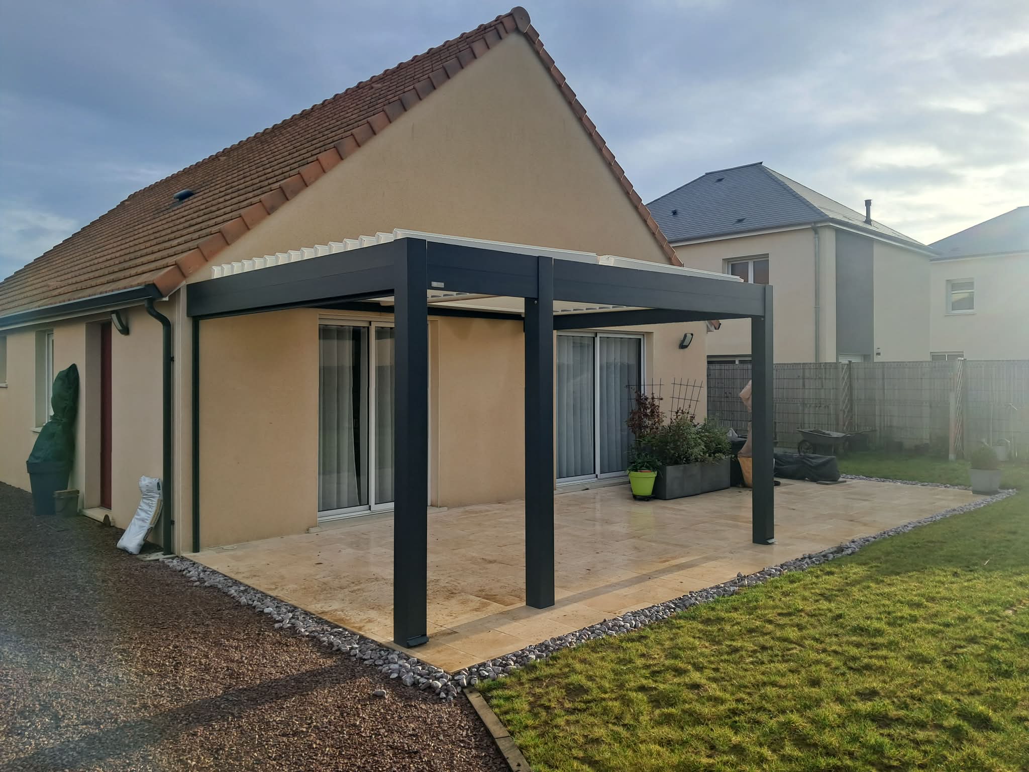 Pergola en aluminium noire avec toiture, installée devant une maison.