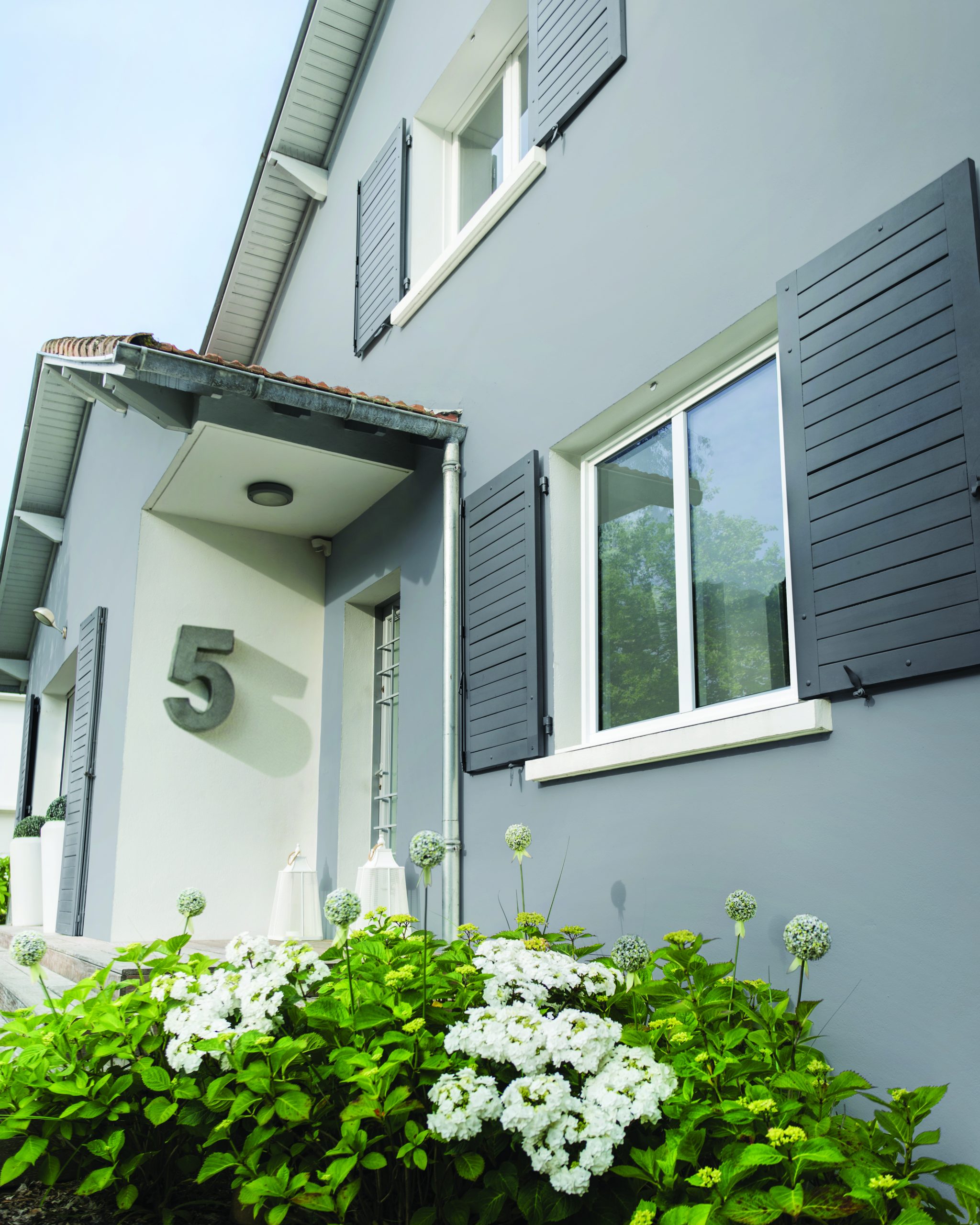 Volet en bois gris foncé installé sur une maison avec fenêtres blanches.