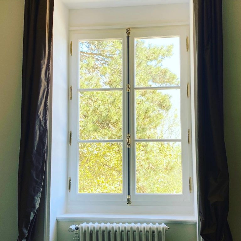 Fenêtre en bois à deux vantaux avec des poignées dorées et des vitres divisées en quatre parties.