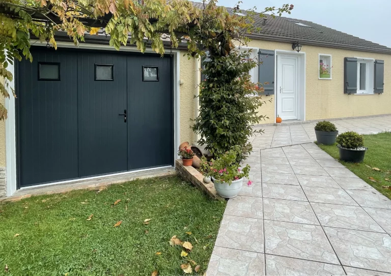 Porte de garage battante en bois peint noir avec fenêtres rectangulaires.