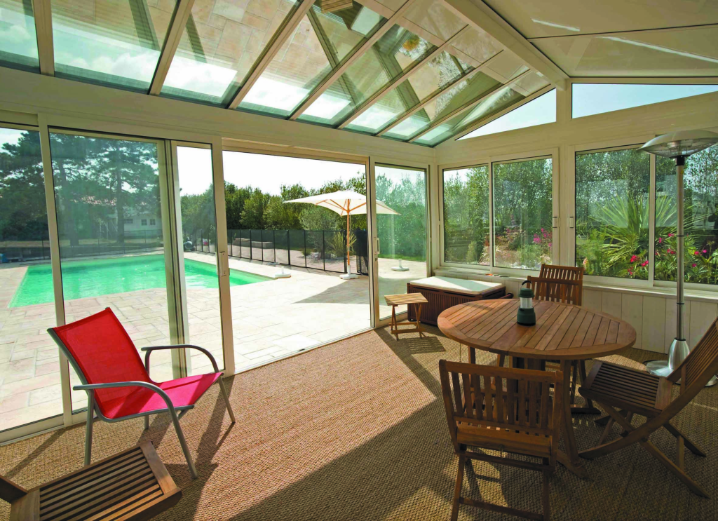 Véranda en PVC avec toit vitré, équipée d'un ensemble table et chaises en bois.