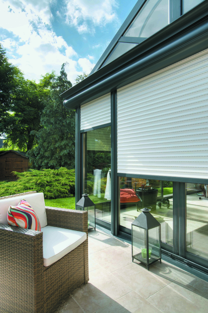 Store enrouleur installé sur une véranda, en tissu blanc, avec structure en aluminium gris.