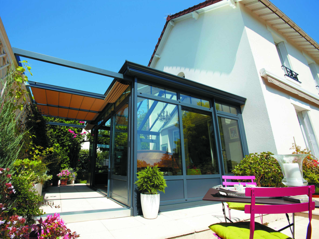 Véranda en aluminium avec toiture vitrée et stores, conçue pour une extension lumineuse.