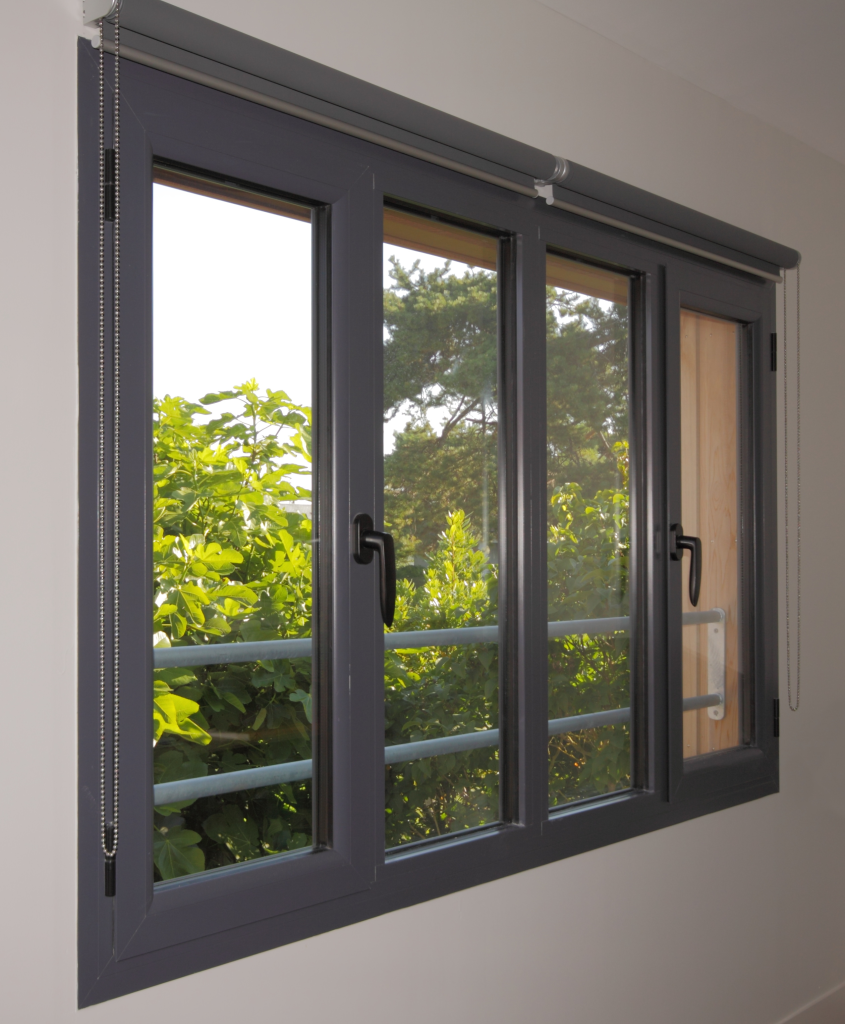 Fenêtre à cadre gris avec volets, équipée de poignées noires, en PVC.
