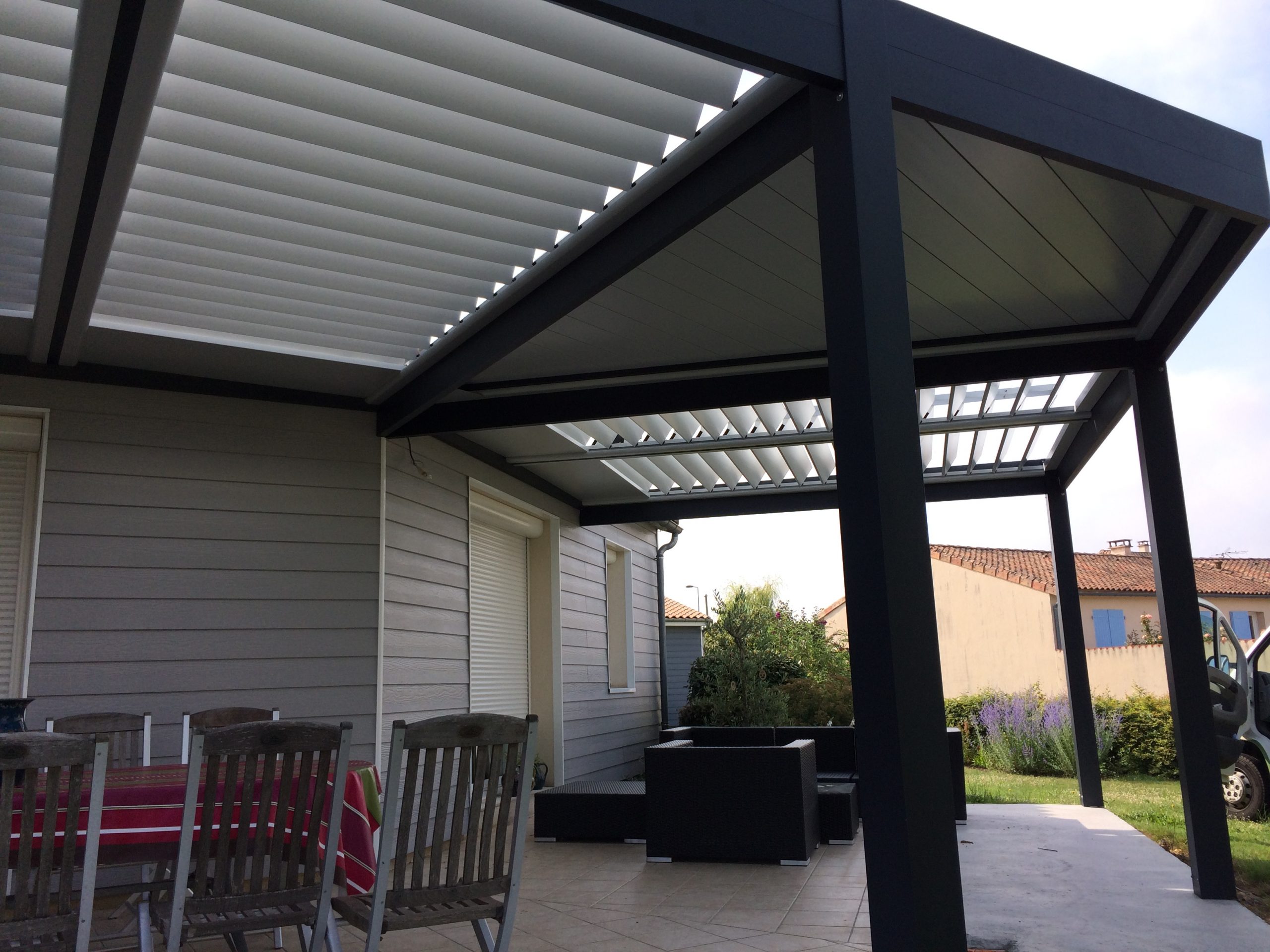 Pergola en aluminium avec lames orientables, installée au-dessus d'un coin salon extérieur, attenant à une maison.