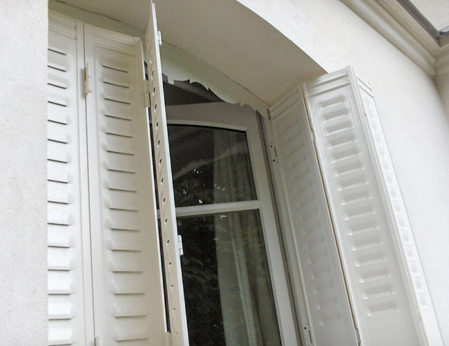 Volet persienné en PVC blanc, installé sur une fenêtre arrondie.
