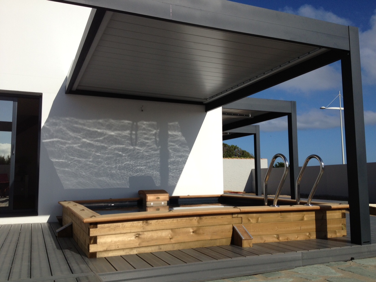 Pergola en aluminium gris avec toiture fixe, surplombant un spa en bois, sur une terrasse en bois.