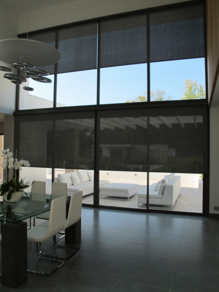 Stores roulants en tissu sombre installés sur de grandes fenêtres.