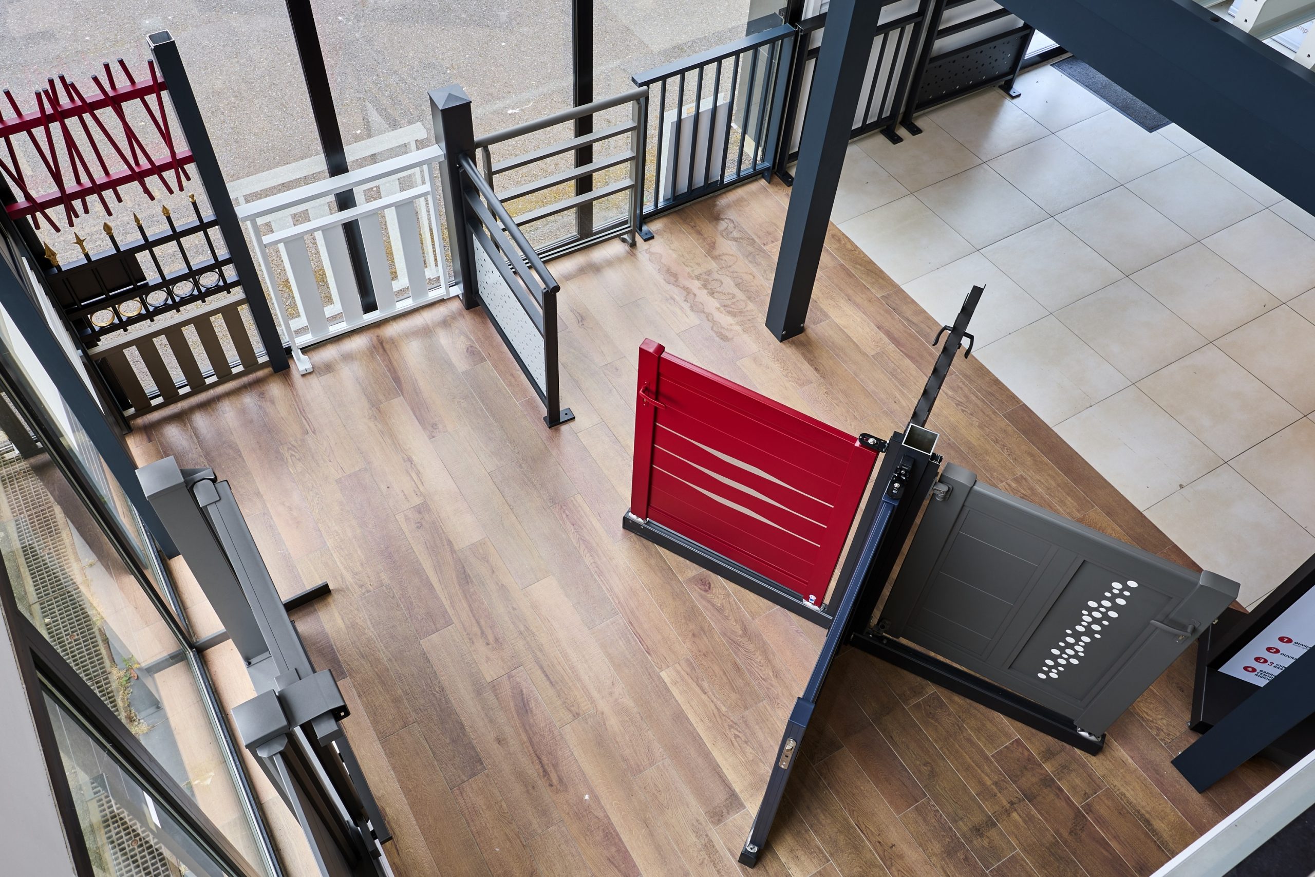 Portails en métal de différents designs, dont un modèle rouge et un modèle gris, présentés dans un espace d'exposition.