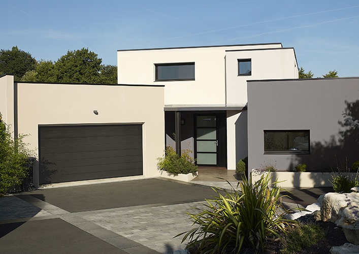 Porte d'entrée en métal gris, fenêtres en verre avec cadres noirs et porte de garage sectionnelle.