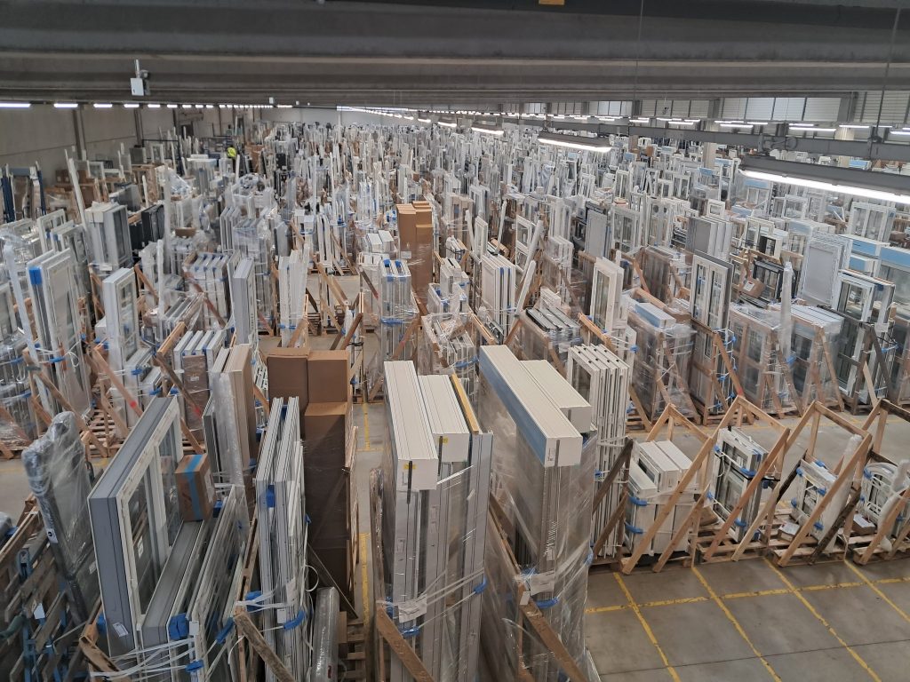 Stock de fenêtres et portes en PVC, toutes emballées et rangées sur des supports en bois.