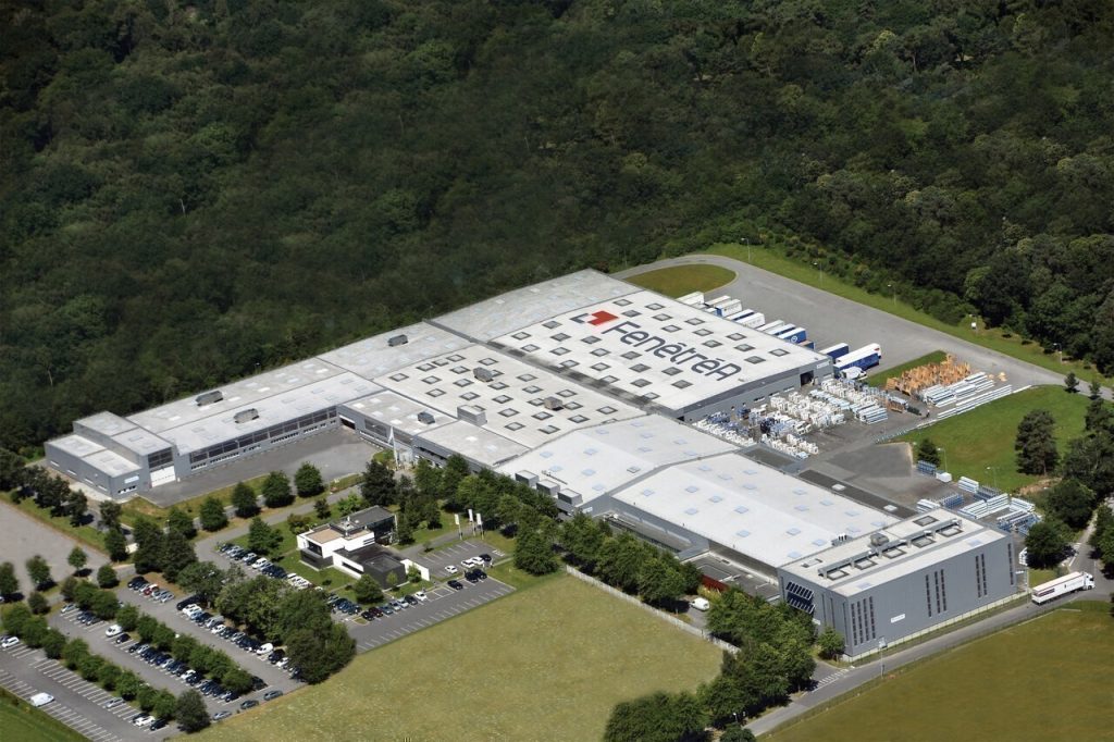 Vue aérienne d'un bâtiment industriel de menuiseries avec matériaux de construction et fenêtres en attente de pose.